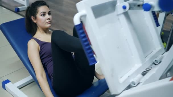 Sports strong girl raises Platform leg press and and gives thumbs-up in sports club — Stock Video