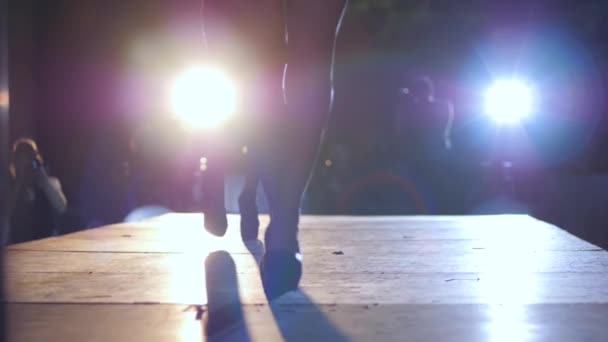 Catwalk modell på högklackat i baddräkt och hatt promenader längs pallen i strålkastare belysning på natten — Stockvideo
