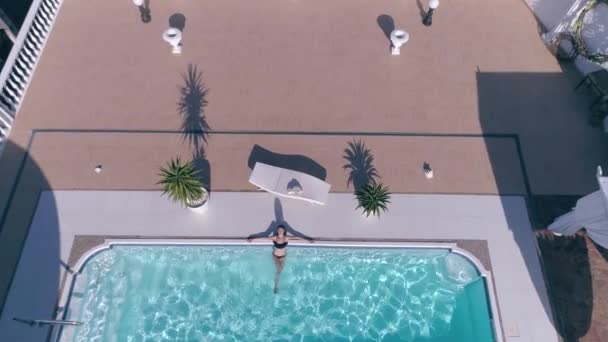 Nettes Mädchen im Badeanzug liegt im blauen Schwimmbad im teuren Sommerurlaub — Stockvideo
