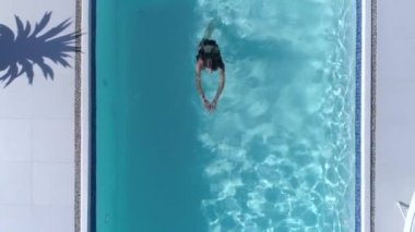 Lüks bir tatil, yaz tatilinde mavi havuz kenarında yüzen mayolu genç bir kadın.