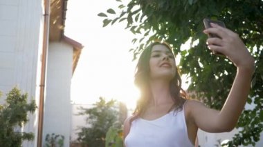 Mutlu güzel bir kız cep telefonuyla fotoğraflandı. Parlak güneş ışığı altında. Yakın plan.
