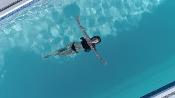 Формально жінка з красивим тілом в купальний костюм відпочиває в блакитному басейні на літніх канікулах — стокове відео