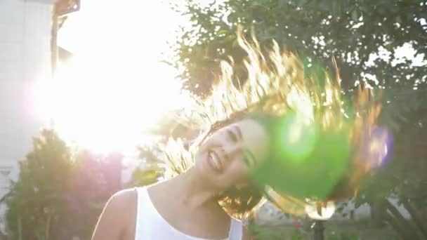 Positiv skrattande flicka viftar hår och roterar i ljus sol belysning utomhus — Stockvideo