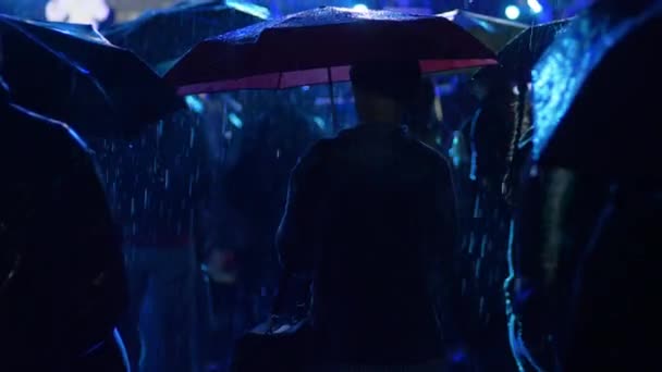 Silhouette femme solitaire sous un parapluie parmi les gens sous la pluie au concert dans les lumières clignotantes — Video