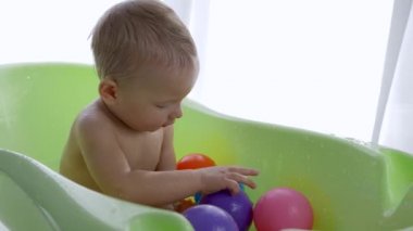 Küçük çocuk bebek banyosunda yüzerken renkli toplarla oynuyor.