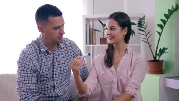 Feliz pareja sana casada con prueba de embarazo aprendido sobre el futuro bebé y abrazar alegremente en la habitación en casa — Vídeo de stock