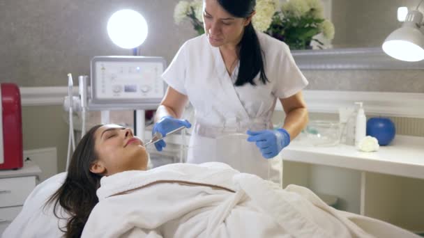 Kosmetyczka wykonuje zabiegi kosmetyczne o działaniu odmładzającym do pielęgnacji twarzy kobiety w salonie spa — Wideo stockowe
