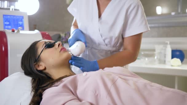 Лазерная эпиляция, специалист-косметолог делает удаление волос на коже пациентки женского пола в салоне красоты — стоковое видео