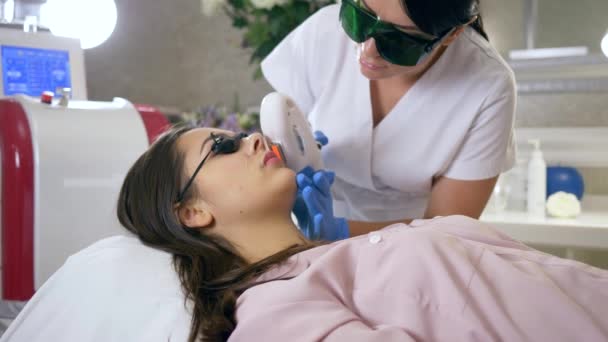 Fotoepilasyon, uzman kozmetik uzmanı, güzellik salonunda lazer aletler kullanan hasta kadının yüzünü temizliyor. — Stok video