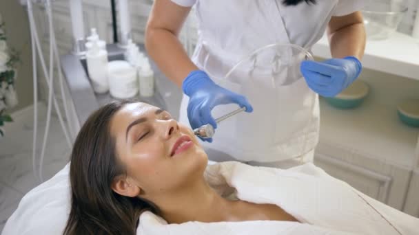 Cuidado de la piel facial, paciente relajante femenina en procedimientos cosméticos estimulación de procesos de renovación en salón de belleza — Vídeos de Stock