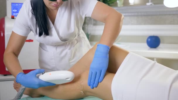 Salud de las mujeres, cosmetólogo utiliza el aparato láser para eliminar el cabello en las piernas de la señora en la sala de tratamiento del salón de belleza — Vídeo de stock