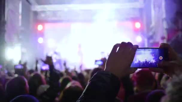 Tłum fanów ze smartfonem w rękach cieszyć się muzyką na żywo na koncercie w żywych świateł scenicznych — Wideo stockowe