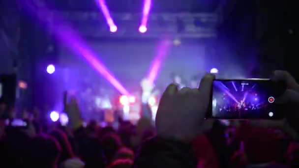 Fans met mobiele telefoons in handen genieten van live muziek op rockconcert in heldere scène lichten — Stockvideo