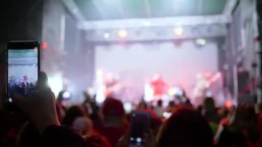 Konserdeki insanlar, gençlik kollarındaki akıllı telefonlar müzik akşamının videolarını çekiyorlar.