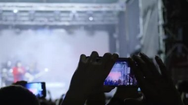 Modern teknolojiler, ellerinde telefon olan hayranlar sahnede rock gösterisinin keyfini çıkarıyorlar.