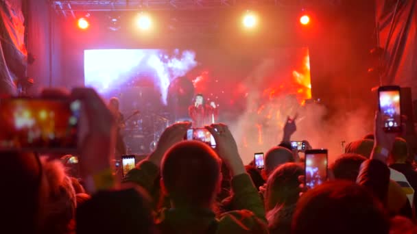 Vrije tijd van de moderne jeugd, mobiele telefoons in handen toeschouwers schieten video van rockconcert op helder verlichte podium — Stockvideo