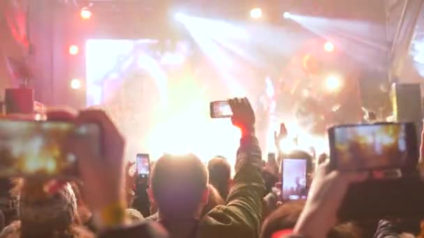Nachtshow, mobiele telefoon in armen van fans schieten video van rockconcert op levendig verlichte podium — Stockvideo