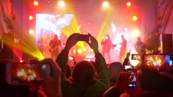 Banda de rock, Muchas manos con el móvil hacer presentaciones de fotos en el escenario iluminado — Vídeos de Stock