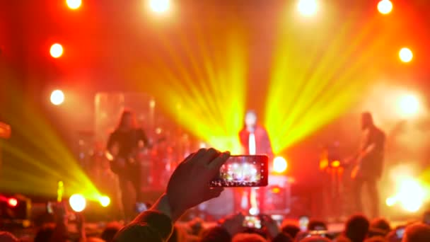 Fã pessoa tirando vídeo e fotos no smartphone móvel na festa de concerto em iluminação de holofotes — Vídeo de Stock