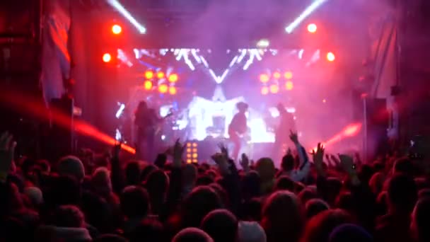 Springen fans met de handen omhoog genot van live muziek van rock band op heldere scène — Stockvideo