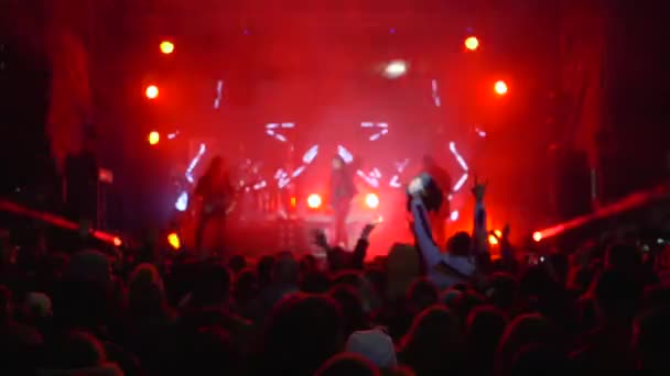 Nachtleven van de jeugd, menigte van de jeugd zwaaien armen omhoog tijdens rockband optreden op het verlichte podium in rook — Stockvideo