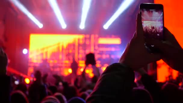 Fan man hace la foto y el vídeo en el smartphone en el concierto de rock en luces intermitentes brillantes — Vídeos de Stock