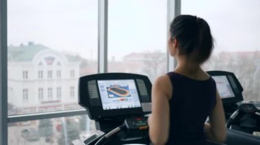 Spor antrenmanı, kız pencerenin arkasındaki modern spor salonunda koşu bandında koşuyor.