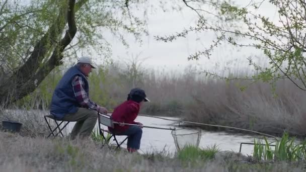 Angeln, Großvater und kleiner Junge fangen kleine Fische mit Angelrute in einer Brustwarze im Fluss — Stockvideo