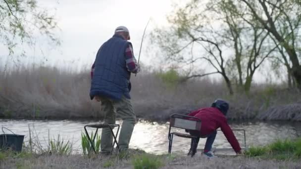 Niño varón feliz con el abuelo de pesca con una caña de pescar en buen tiempo de primavera — Vídeos de Stock