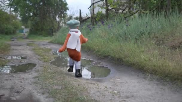 Crianças felizes brincando, menino bonito correndo se divertindo pulando através de poças de botas de borracha em uma estrada rural — Vídeo de Stock