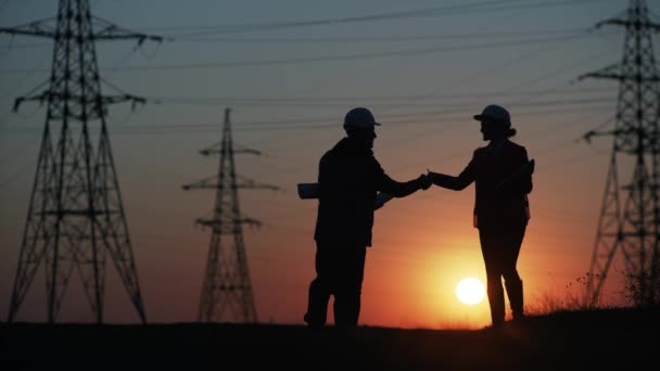 Técnico cascos protectores masculinos y femeninos con dibujos y portátil en las manos discutir la construcción de torres de alta tensión y torres de transmisión, silueta — Vídeos de Stock