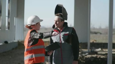 Koruyucu miğfer ve çizimler yapan kadın mühendis ve koruyucu giysi ve kask konusunda uzman bir erkek hangarın yapımında görevli.