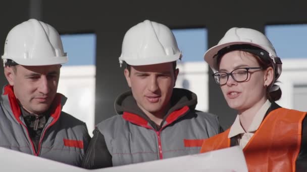 Barátságos csapat férfi és női szakértők az építőiparban biztonsági sisakok megvitatják rajzok — Stock videók