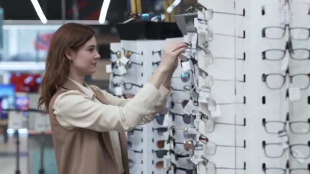 Zakupoholiczka, stylowa młoda kobieta shopper, kupujący wybiera okulary przeciwsłoneczne na półkach sklepu — Wideo stockowe