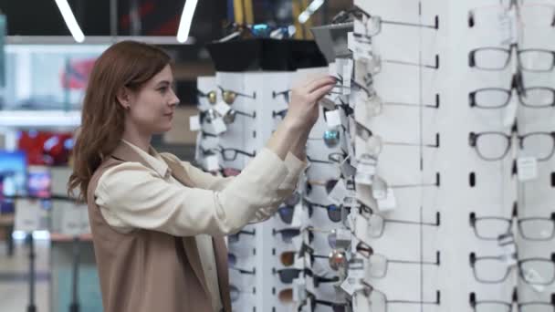 Shopaholic, stijlvolle jonge vrouw shopper, koper kiest zonnebril op rekken van de winkel — Stockvideo