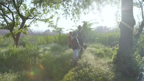 В теплый солнечный день маленькие веселые дети с заботливой бабушкой и дедушкой веселятся на свежем воздухе среди деревьев — стоковое видео