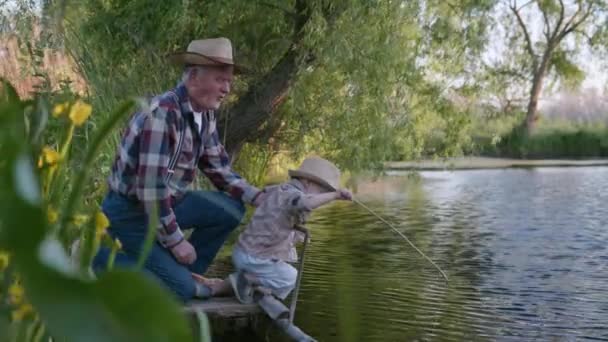 Barndom, liten söt hane barn tillsammans med sin älskade farfar, fiskare lär sig att fiska i damm med fiskespö — Stockvideo