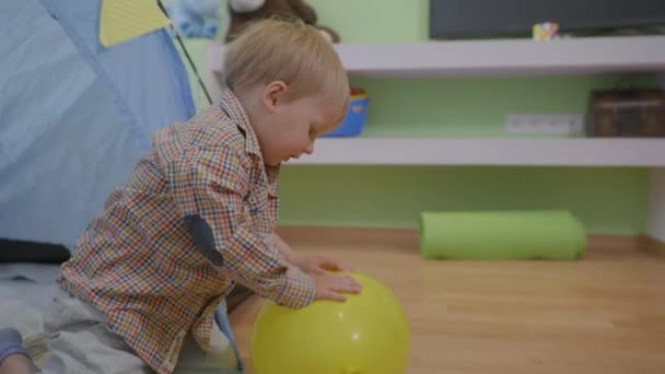 Alegre criança feliz se divertindo desfrutando de um jogo de um balão enquanto sentado — Vídeo de Stock