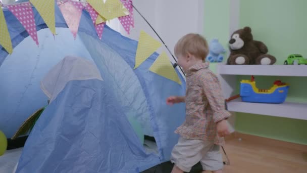 Беззаботное детство, дети играют в прятки в комнате, дружелюбный красивый мальчик в карнавальном костюме весело играет со своим младшим братом в вигваме — стоковое видео