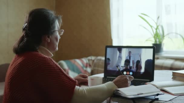 Enseñanza a distancia, abuela moderna pasa por la enseñanza a distancia durante la conferencia en línea mediante videollamada en el ordenador portátil — Vídeo de stock