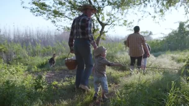 Семейный отдых, заботливый дедушка со своей престарелой возлюбленной женой и счастливыми внуками гуляют на свежем воздухе среди деревьев и зеленой травы — стоковое видео