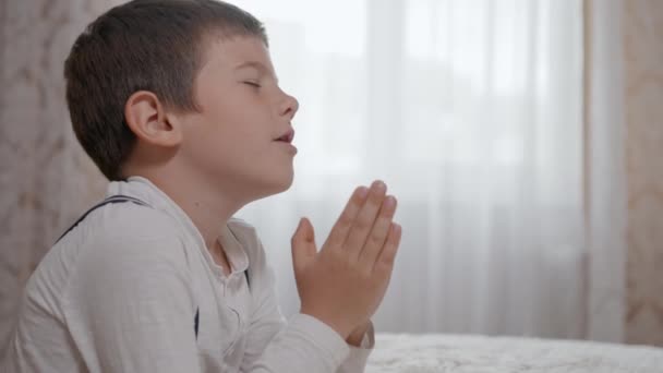 Religião, oração criança masculina confiar em Deus com esperança em seu coração e com os braços dobrados juntos em pé sobre rodas perto de cabeceira — Vídeo de Stock