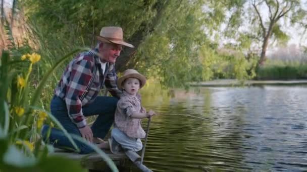 Idoso velho homem brincando com neto no cais por rio enquanto relaxa na natureza entre juncos — Vídeo de Stock