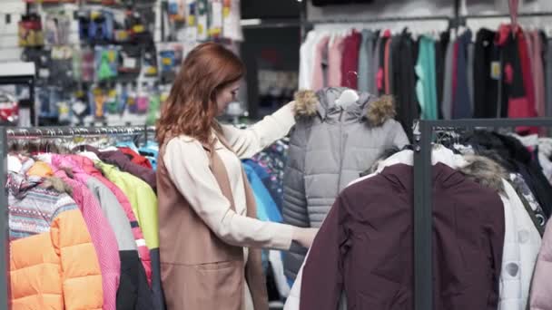 買い物客でチャーミングな笑顔の若い女性ファッション店で美しいジャケットを試着するのが好き — ストック動画