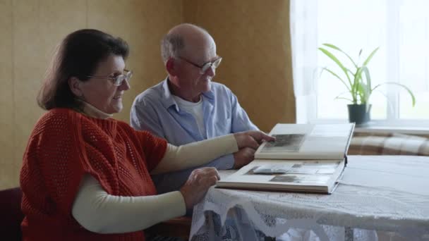 Senioren-Paare, die Liebe und Fürsorge füreinander bewahren, lassen sich von Erinnerungen an vergangene Jahre inspirieren und betrachten Fotos im Familienfotoalbum — Stockvideo