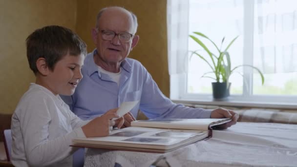 Familie herinneringen, kleine schattige jongen met zijn bejaarde grootvader veel plezier kijken naar een oud fotoalbum — Stockvideo