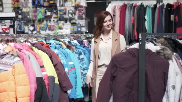 Winkelen en verkoop, vrouwelijke koper kijkt naar hanger modieuze dingen in kledingwinkel — Stockvideo