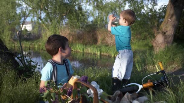 Sommarsemester, glada bekymmerslösa manliga barn ha kul utomhus och hungrig dricka hälsosam mjölk och bröd på en picknick — Stockvideo