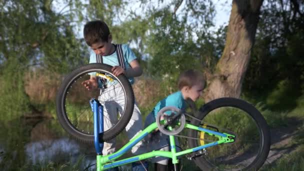 Attractive curious boys spin wheels and pedals of bicycle while having fun outdoors by river — Stock Video