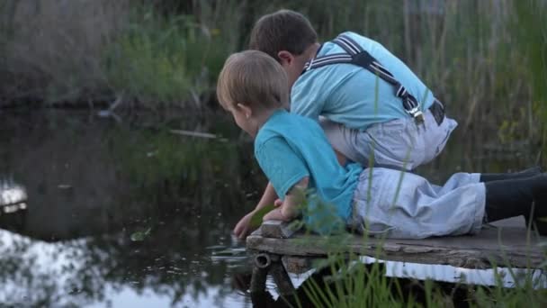 Outdoor activiteiten, leuke jongens broers hebben plezier op pier in de buurt van de rivier en spelen in het water met bladeren, kleine mannelijke kinderen spelen door vijver — Stockvideo